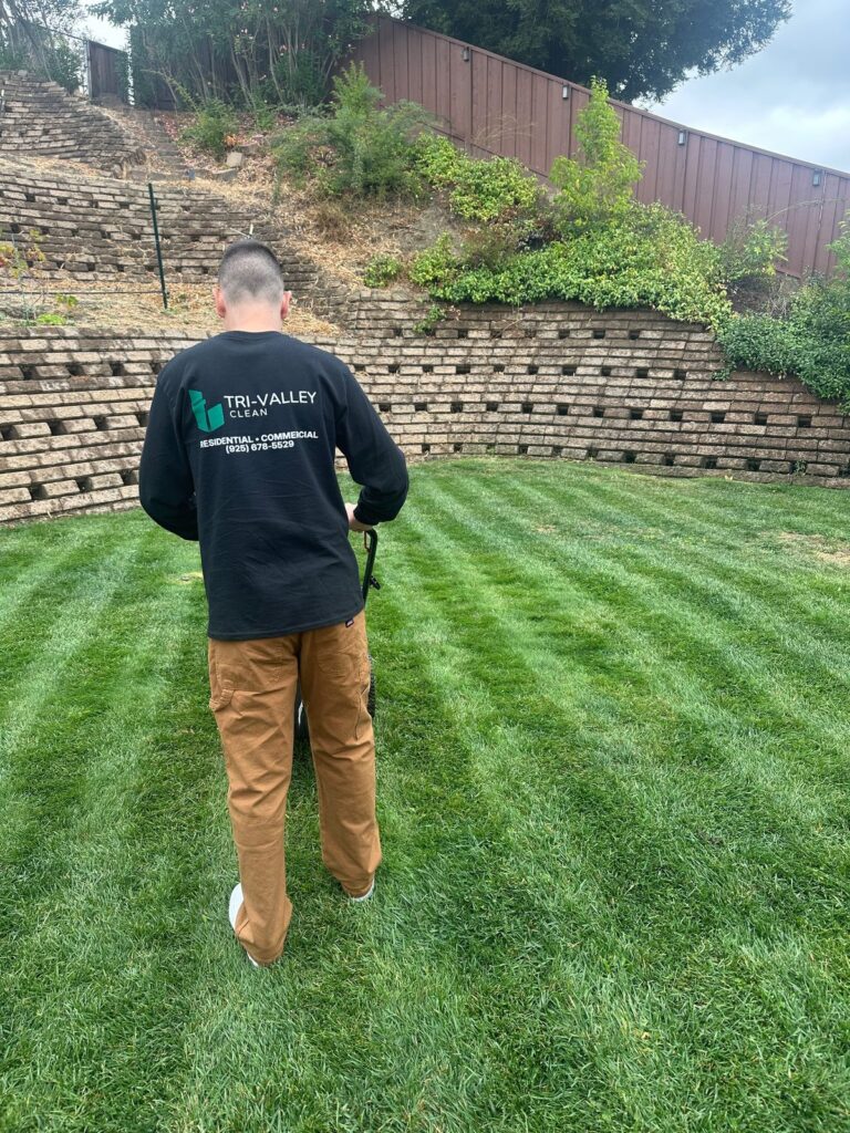 Tri-Valley Clean team member mowing a backyard lawn